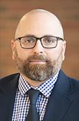 Headshot of Michael Jacobs with glasses and a beard, wearing a suit and tie.